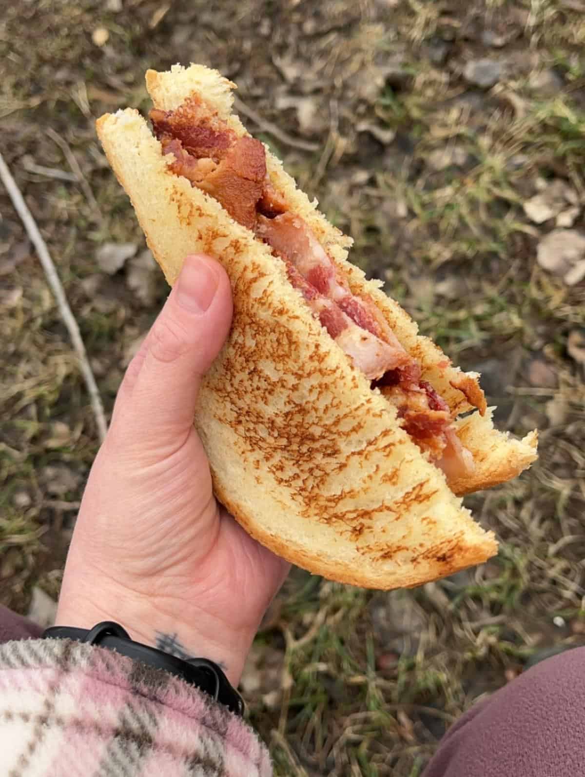 A woman's hand holds up a bacon sandwich on white bread.