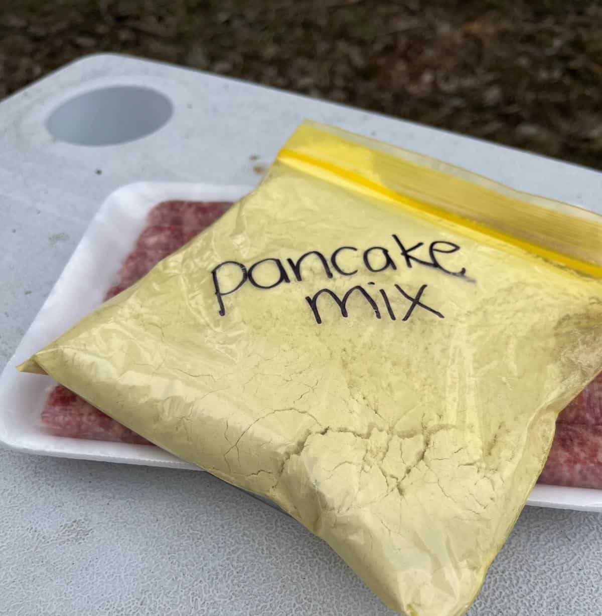 A Ziploc bag full of homemade pancake mix rests on a package of breakfast sausages on top of a cooler.