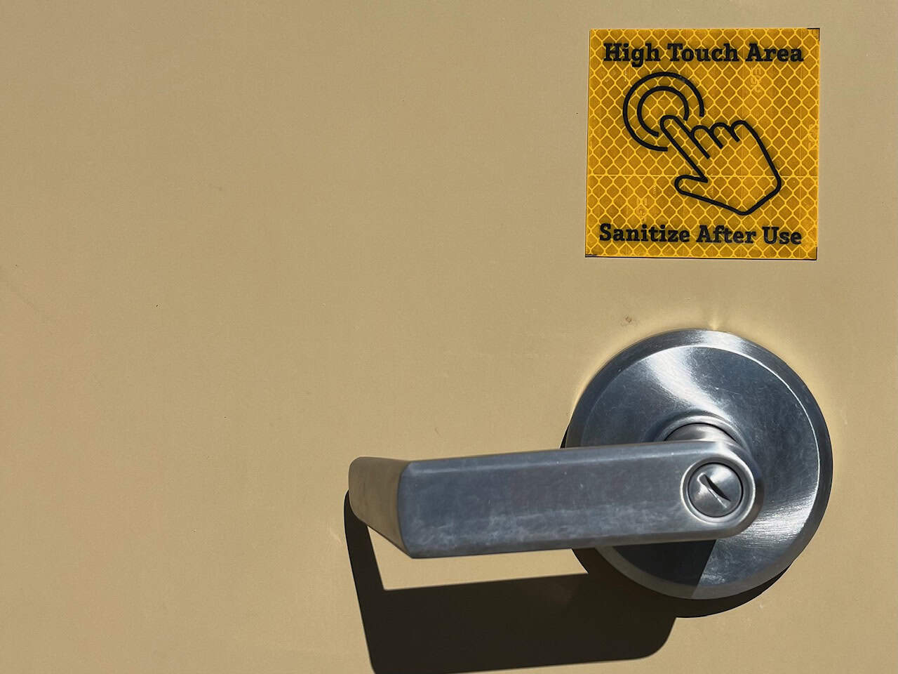 The door to an outhouse. Above the doorknob, there is a sticker that says "High touch area, sanitize after use".