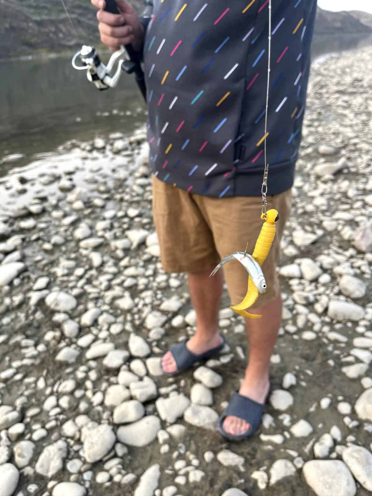 A man holds a fishing line with a small fish attached as bait.