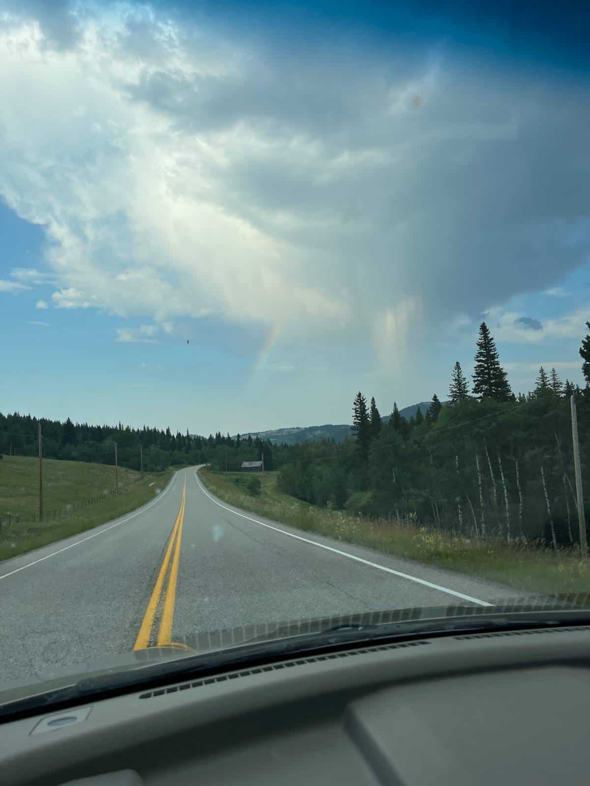 A drive through the hills with a rainbow over the road.