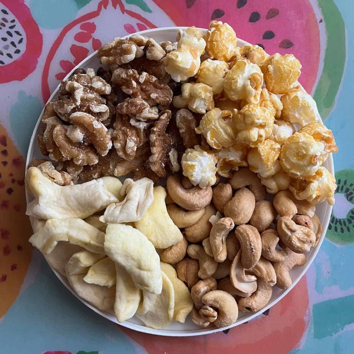 A plate with walnuts, dried apple rounds, cashews, and caramel popcorn.