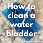 This is the title image. A dish scrubbing brush lays on a water bladder. The words "how to clean a water bladder" are overlaid on the image.