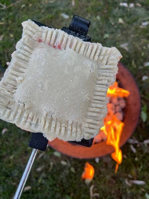 A pie iron over a fire with a pastry waiting to be cooked.