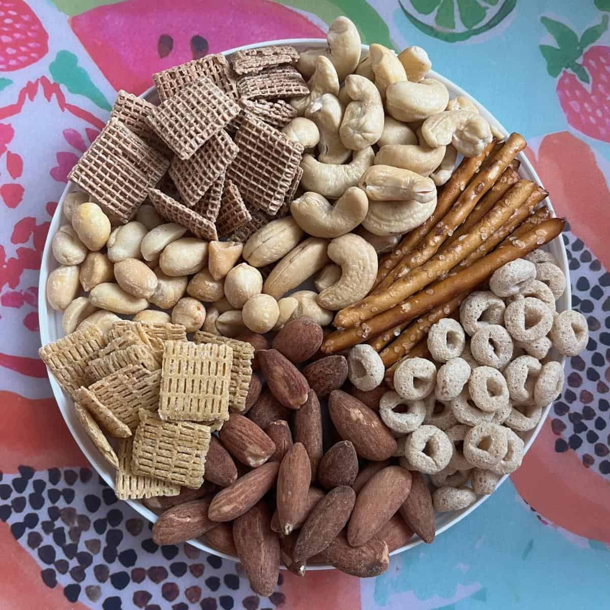 A plate with Shreddies, cashews, pretzels, Cheerios, almonds, Chex Mix, and peanuts.