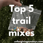 This is the title image. A woman's hand holds up a baggie full of trail mix. The words "top 5 trail mixes" are overlaid on the image.