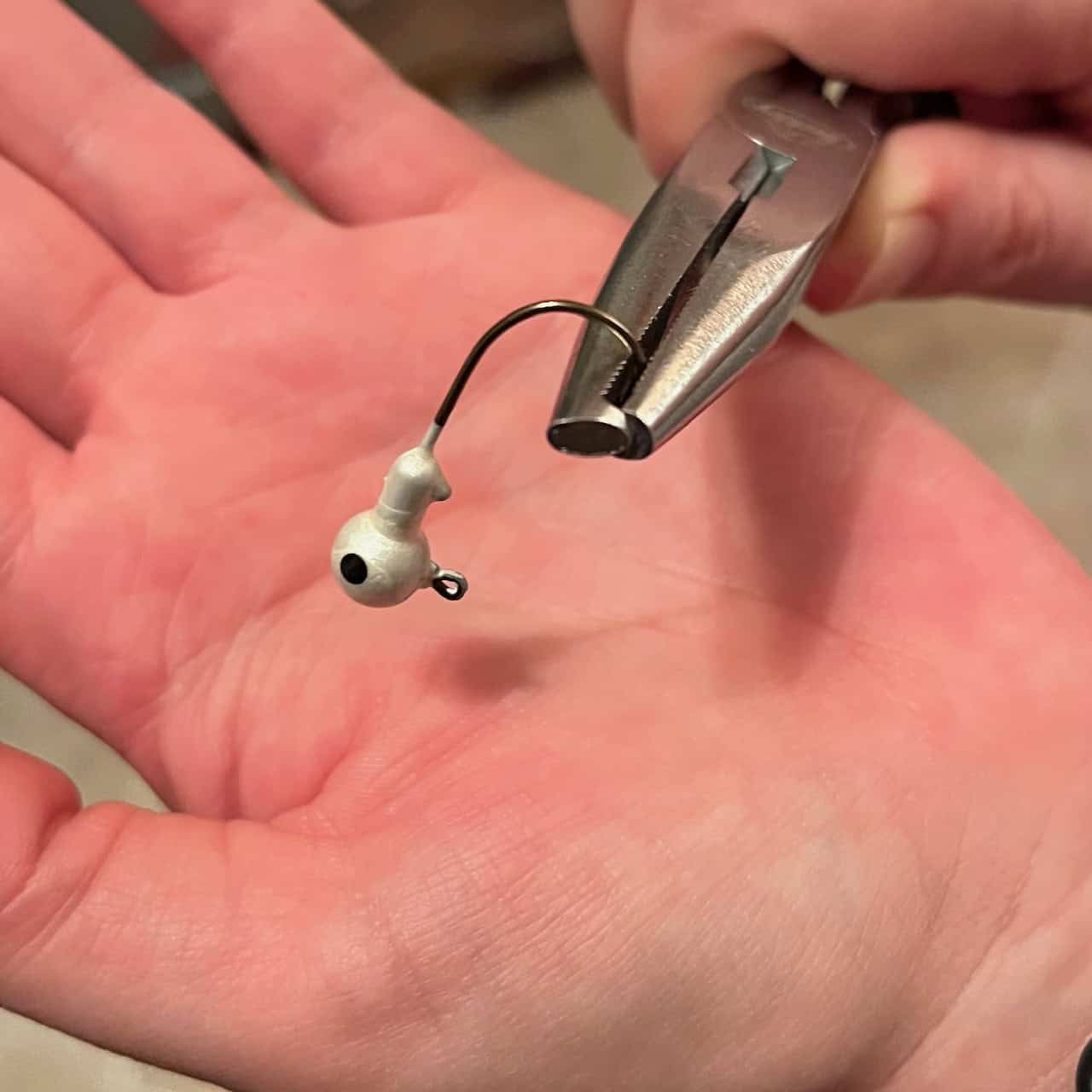 A pair of needle-nosed pliers crimping the barb on a fishing hook.