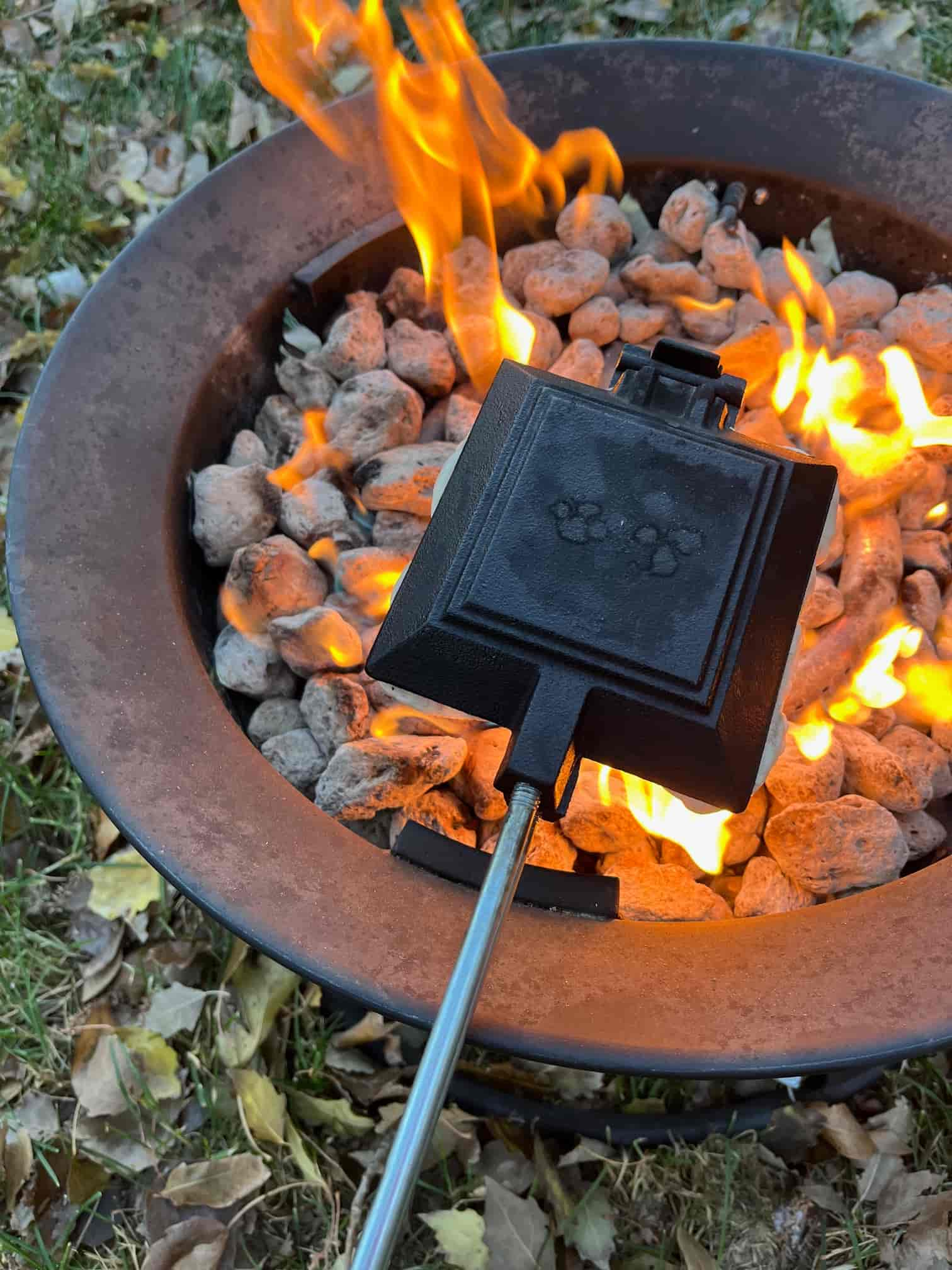 A pie iron containing a campfire pizza pocket is held over a fire.