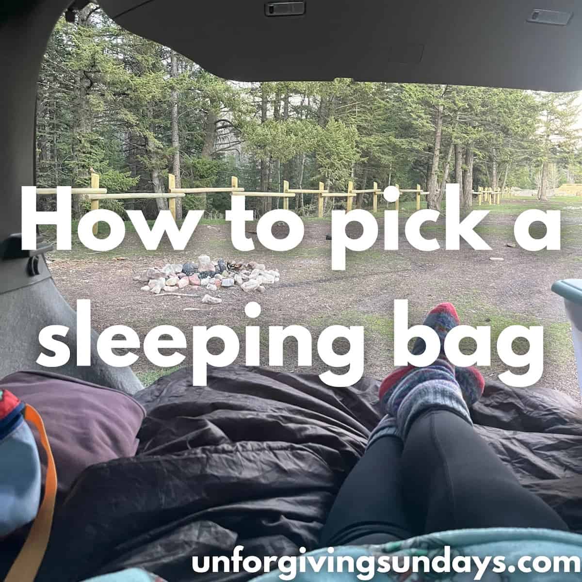 This is the title image. A woman lays on her sleeping bag in the back of her car, looking out the back at the forest. The words "how to pick a sleeping bag" are overlaid on the image.